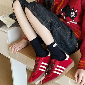 Red suede sneakers with white stripes and black mid-calf socks for a vintage look