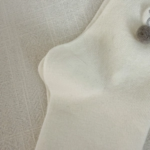Detailed macro view of cream knitted socks featuring a soft grey pom-pom and fine texture