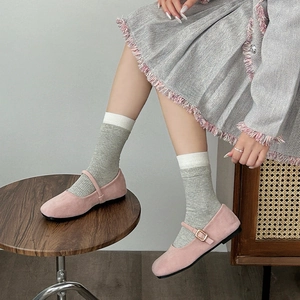 Pink suede Mary Jane flats with metal buckle and grey knit socks on wooden platform