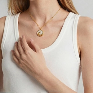 Detailed view of wave-patterned shell pendant on a dainty gold-plated beaded chain necklace