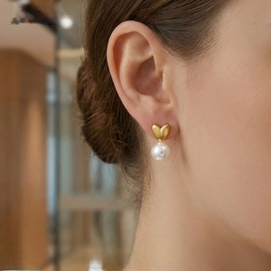 Detail view of heart-shaped gold studs with elegant white round pearls on ear