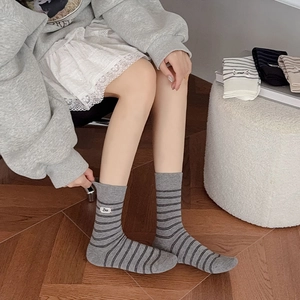 Dettaglio calze a righe in cotone grigio con etichetta Bee su pavimento in legno