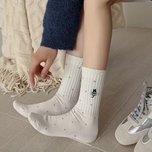 Detailed close-up of white crew socks with grey polka dots and black cat embroidery