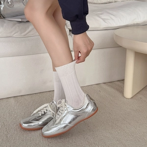 Silver metallic retro sneakers styled with white ribbed mid-calf socks in home setting