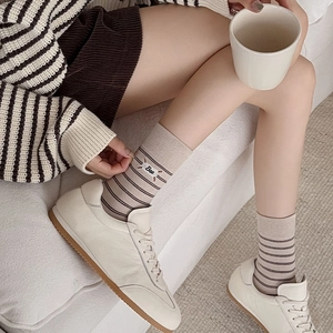 Dettaglio di calze a righe color avena con ricamo Bee e scarpe da ginnastica bianche
