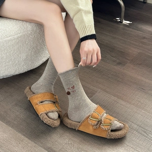 Detail of grey socks with cute cat embroidery and pom-poms paired with camel fur slippers