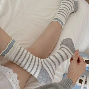 Close-up of grey and white striped crew socks with ruffled cuffs on a soft white bed