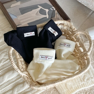 Detail of knitted ribbed crew socks featuring fabric labels and bow patterns in a basket