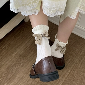 Nahaufnahme weißer Rüschensocken mit brauner gepunkteter Schleife und Schuhen