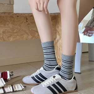 Macro detail of grey striped crew socks paired with vintage suede sneakers on wood floor