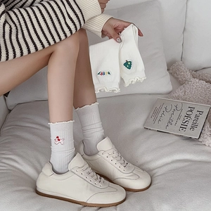 Détail de chaussettes à volants blanches brodées et baskets en cuir blanc cassé