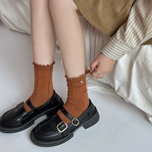 Detail of rust red ruffle edge socks paired with black double buckle Mary Jane shoes
