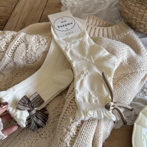Detail von cremefarbenen Stricksocken mit braunen Karoschleifen und Rüschenbündchen