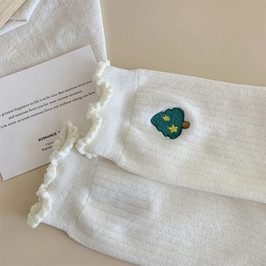 Détail de chaussettes blanches avec bords volantés et broderie d'arbre vert mignon