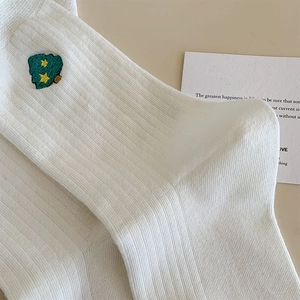 Détail de chaussettes blanches en coton côtelé avec broderie sapin de Noël et étoiles jaunes