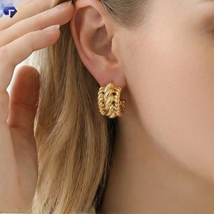 Close-up of a wide twisted gold hoop earring with a braided rope texture on a model