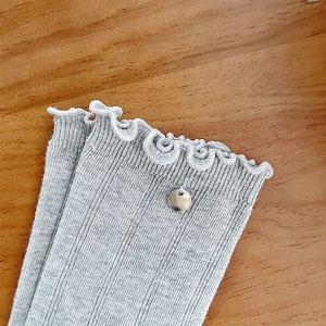 Detail of grey ribbed knit socks featuring ruffled edges and a silver metal pendant accent