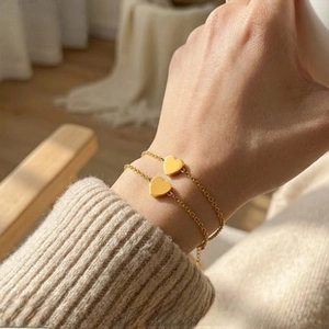 Close-up of golden stainless steel heart pendant bracelets worn on a wrist in a cozy setting