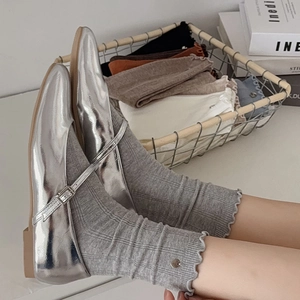Detail von Socken mit Rüschensaum und Metallemblem zu silbernen spitzen flachen Schuhen