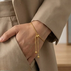 Close-up of golden snake chain bracelet featuring a central knot and polished bead charms