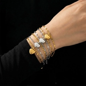 Macro detail of gold and silver heart pendants on layered titanium steel chain bracelets