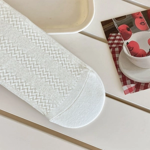 Close-up of white knit socks featuring fine herringbone pattern on a cream tabletop
