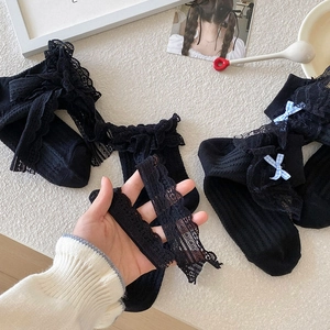Detail von schwarzen Lolita-Spitzensocken mit Rüschen und blau-karierten Schleifen