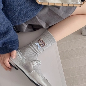 Detail of grey socks with cat embroidery and bow paired with silver Mary Jane shoes