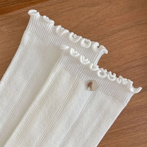 Detail von weißen Rippstricksocken mit Wellensaum und einem silbernen Metallanhänger