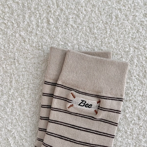 Detailed close-up of striped knit socks featuring Bee embroidery on warm sherpa background