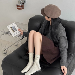 Detail of off-white knit socks with dark speckles and a wavy lettuce trim cuff
