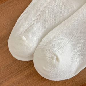 Detailansicht weißer gerippter Stricksocken mit nahtloser Spitze auf Holzstruktur