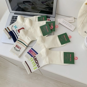 Detail of cream cotton crew socks featuring colorful stripes and embroidered varsity letters