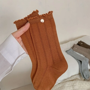 Makro-Detail von karamellfarbenen Socken mit Rüschenkante und dekorativem Metallknopf