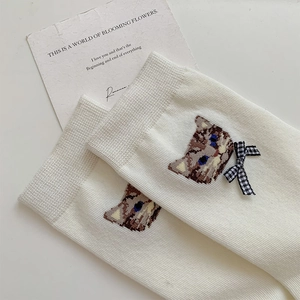 Close-up of white knit socks featuring embroidered cat pattern and black-white plaid bow