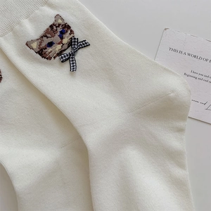 Close-up of white cotton socks with cat embroidery and a checkered bow detail