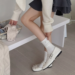 Nahaufnahme weißer Mary Jane Lederschuhe mit Metallschnallen und Socken mit Rüschen