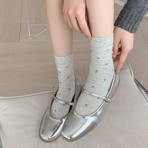 Floral knit crew socks paired with silver metallic Mary Jane flats on wood flooring