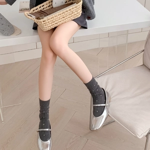 Detail of dark grey polka dot socks paired with shiny silver Mary Jane shoes in soft light