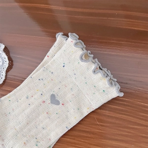 Macro detail of cream knit socks with colorful confetti spots and gray lettuce edge cuffs