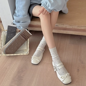 Close-up of off-white Mary Jane shoes with floral embroidery socks on wooden stairs