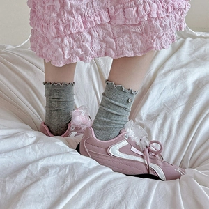 Detail of pink sneakers with organza bows and ruffled grey socks on white fabric