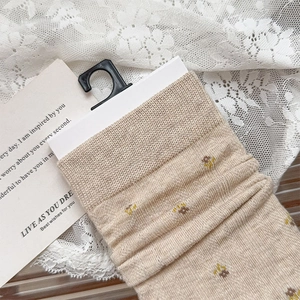 Detail of floral embroidery and ribbed cuff on beige crew socks with hook packaging