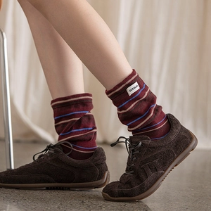 Detail of burgundy striped knit socks with brand label worn with brown suede sneakers