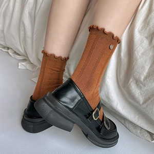 Orange frilly socks with metal button and black platform Mary Janes on white fabric
