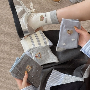 Detail of cute bear embroidery and striped pattern on blue and grey cotton crew socks