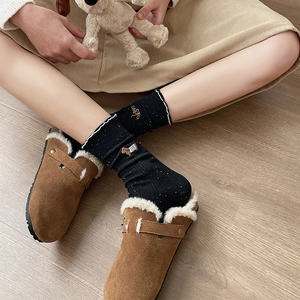Close-up of black knit socks with cute embroidery and ruffled cuffs worn with brown clogs
