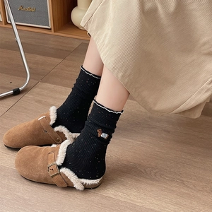 Detail of knit socks with bear embroidery and brown plush slippers on wooden floor