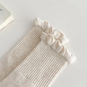 Macro detail of cream white ribbed socks featuring ruffled lettuce edges and knit texture