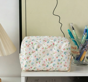 Quilted floral makeup bag detail showing white zipper and pink flower pattern on desk